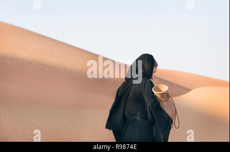 Jeune femme en robe traditionnelle abaya (espagnol) dans un désert pour transporter de l'eau Banque D'Images