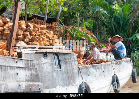 Quatre hommes ayant une pause sur un bateau traditionnel en bois avec des cocotiers le long de la rive bordée d'sur la rivière Cai Rang, Province de Can Tho, Vietnam du Sud Banque D'Images