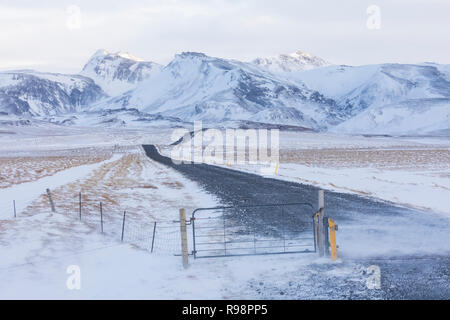 La neige poussée par le vent sur une route en direction de la montagne près de la calotte glaciaire de Mýrdalsjökull et la ville de Vik, en hiver en Islande Banque D'Images