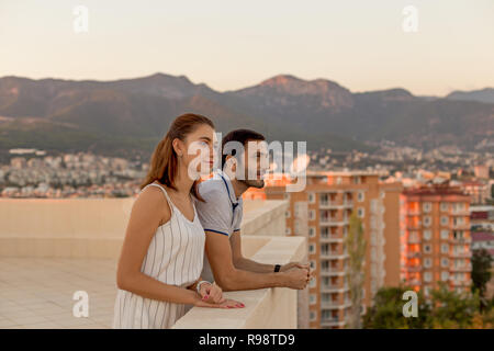 Jeune couple en tenue d'été bénéficiant d'une vue sur la ville et la montagne à partir de la terrasse sur le toit. Plan horizontal. Banque D'Images