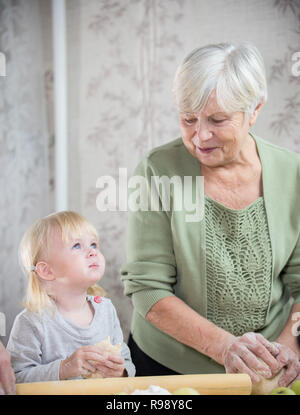 Bénéficiant d'une vieille femme faisant peu de tartes aux pommes avec sa petite-fille. Une petite fille enduite de farine Banque D'Images