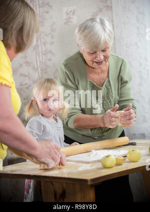 Bénéficiant d'une vieille femme faisant peu de tartes aux pommes avec sa petite-fille. Surpris petite fille enduite de farine Banque D'Images