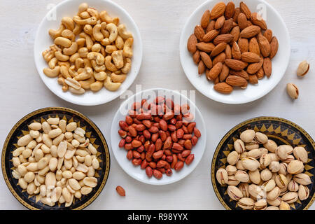 Les écrous frais dans des bols d'arachides, arachides, noix de cajou, Amandes et pistaches (vue de dessus sur un tableau blanc dans un régime alimentaire sain concept Banque D'Images