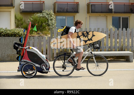 Surfer riding bike avec planche de surf et de remorquage remorque enfant à Wissant dans le nord de la France Banque D'Images