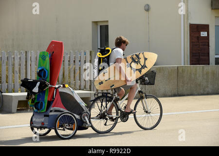 Surfer riding bike avec planche de surf et de remorquage remorque enfant à Wissant dans le nord de la France Banque D'Images