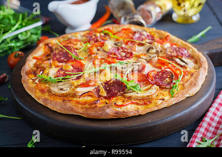 Pizza italien frais avec filet de poulet, champignons, jambon, salami, fromage, tomates sur un fond noir. Cuisine italienne. Banque D'Images