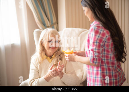 Heureux mère âgée prend son anniversaire Muffin avec bougie brûlante de sa fille des mains. Brunette fille célèbre sa vieille mère. Banque D'Images