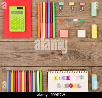 Jeu de l'école avec l'inscription de 'back to school', calculatrice, bloc-notes, marqueurs et autres articles de papeterie sur table en bois brun Banque D'Images