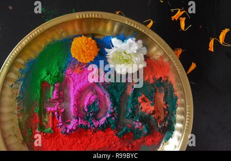 Le mot "Holi" écrit en poudre colorée dans une plaque en laiton et fleurs-Holi festival/Inde Banque D'Images