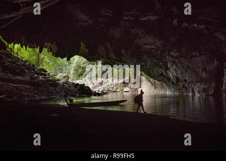 Silhouette d'une femme marche par la rive du fleuve à l'entrée de la grotte de Konglor au Laos Banque D'Images