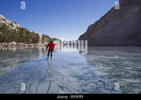 Man in red jacket patinage sur lac gelé le Loch Leven dans les montagnes de la Sierra Nevada Banque D'Images