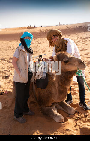 La province d'Errachidia, Maroc, l'Erg Chebbi, l'homme avec la préparation de chameau pour rouler dans le désert de dunes de sable Banque D'Images