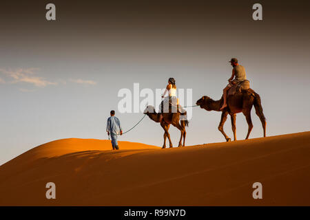 La province d'Errachidia, Maroc, l'Erg Chebbi, les touristes sur les chameaux à travers les dunes au coucher du soleil Banque D'Images