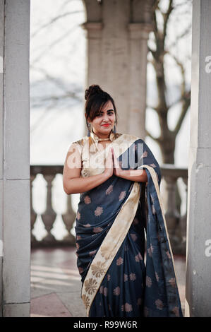 Elegant brunette fille indienne de l'Asie du sud en saree debout sous arch et montrer namaste mains signe. Banque D'Images