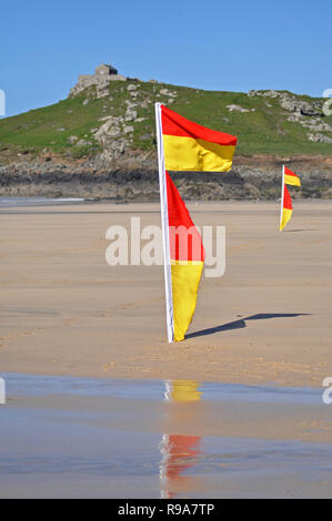 Lifeguard les drapeaux sur la plage de surf Porthmeor reflétant dans le sable humide avec en arrière-plan de l'île et ciel bleu St Ives Cornwall UK Banque D'Images