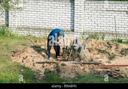 Homme avec une hache déracine une souche d'arbre sur une journée d'été Banque D'Images