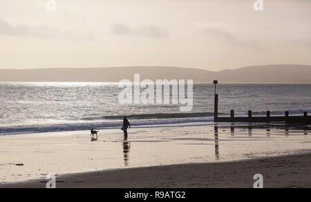 Bournemouth, Dorset, UK. 22 décembre 2018. Les visiteurs à profiter du soleil des plages de Bournemouth, échapper à l'agitation de dernière minute achats de Noël et les préparatifs. L'homme jouant avec chien sur le bord de la mer se découpant dans la lumière du soleil. Credit : Carolyn Jenkins/Alamy Live News Banque D'Images