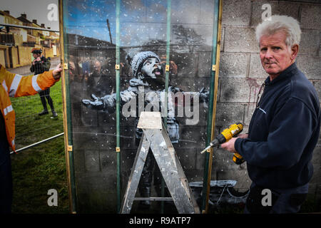 Port Talbot, Pays de Galles, Royaume-Uni. 22 Décembre 2018 Une œuvre de célèbre artiste de rue, Banksy, a été recouverte d'une couverture de protection en plastique, dans la Galles du sud ville de Port Talbot. L'art, montre un enfant se couvrir de cendres d'un bac de gravure et a attiré des milliers de visiteurs depuis en a été confirmée comme étant l'accomplissement de l'artiste, Bristol l'action de l'OMS a atteint des centaines de milliers de livres aux enchères. Crédit photo : Robert Melen/Alamy Live News Banque D'Images