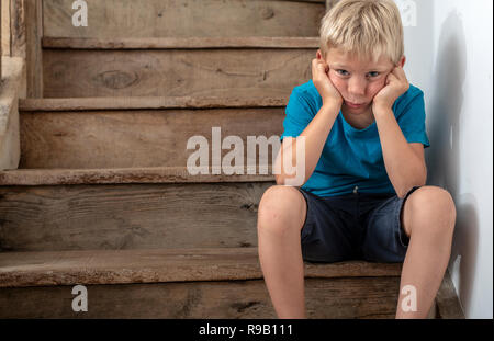 Jeune garçon assis sur l'escalier dans l'angle, en colère ou triste. Banque D'Images