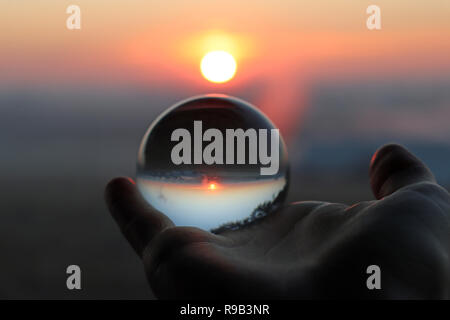 Main tenant une boule de cristal Photographie reflétant une rose orange sunrise Banque D'Images