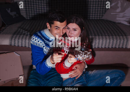 Jeune couple watching movie eating popcorn at home la nuit. Peuple excité pointant à l'écran Banque D'Images