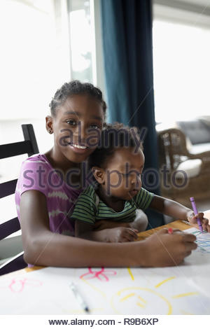 Portrait of smiling girl holding frère à genoux et la coloration à table