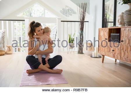 Affectueux mother holding baby daughter on yoga mat