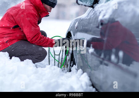 Jeune homme hiver mettre les chaînes sur voiture sur une journée froide Banque D'Images