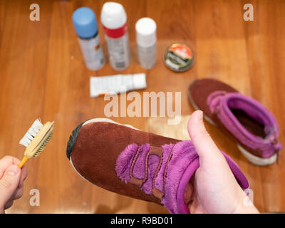 Chaussures en daim de womans dans une main et le pinceau dans l'autre. Soin produit set brouillé sur background, selective focus on foreground Banque D'Images