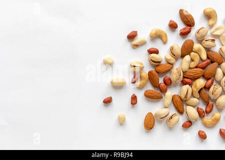 Un assortiment de noix rôties et dispersés sur blanc aux amandes, arachides, arachides, pistaches et noix de cajou vue dans un appartement au-dessus de la vie encore laïcs Banque D'Images