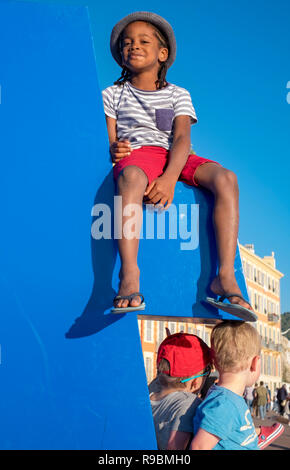 Jeune fille noire dans un chapeau et short rouge est assis sur un affichage public sur une journée ensoleillée à Nice, France Banque D'Images