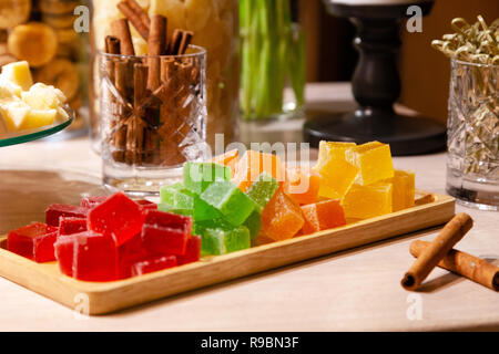 Libre de piles de petits cubes de vert, rouge, jaune, la marmelade d'orange et des bâtons de cannelle dans le verre cristal sur la plaque en bois rectangulaire sur un caterin Banque D'Images