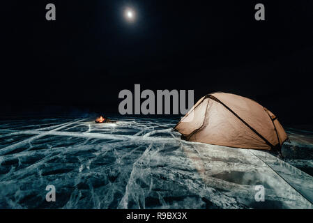 Le feu sur la glace la nuit. Camping sur la glace. Se trouve à côté de la tente de joie. Le lac Baïkal. Tout près il y a voiture. Tente abri et de glace sont éclairés de l'intérieur. Belle joie sur la glace fissurée réel. Banque D'Images