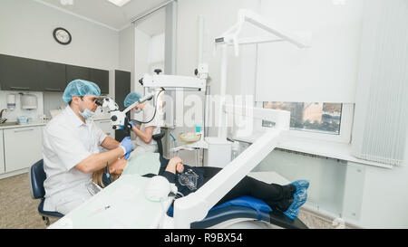 Médecin utilisé microscope. Dentiste est de traiter le patient en cabinet dentaire moderne. L'opération est réalisée à l'aide de batardeau. Client est inséré et dents restaurées, faire remise. Banque D'Images