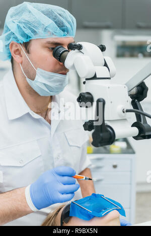 Médecin utilisé microscope. Dentiste est de traiter le patient en cabinet dentaire moderne. L'opération est réalisée à l'aide de batardeau. Client est inséré et dents restaurées, faire remise. Banque D'Images
