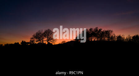 Vue aérienne d'un spectaculaire coucher de soleil derrière des belles montagnes et la silhouette de quelques arbres au premier plan. Banque D'Images