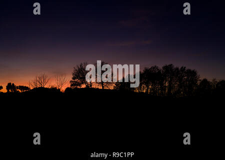 Vue aérienne d'un spectaculaire coucher de soleil derrière des belles montagnes et la silhouette de quelques arbres au premier plan. Banque D'Images