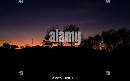 Vue aérienne d'un spectaculaire coucher de soleil derrière des belles montagnes et la silhouette de quelques arbres au premier plan. Banque D'Images