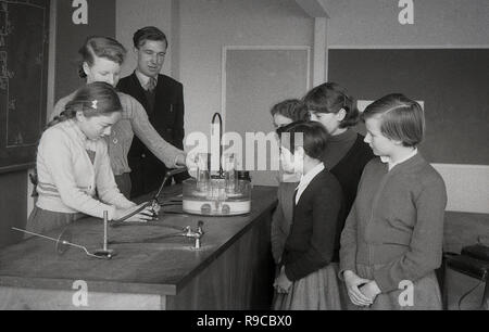 1955, une lycéenne faisant une expérience à un établi dans la classe des sciences, aidé par un enseignant et surveillé par ses camarades élèves, England, UK Banque D'Images