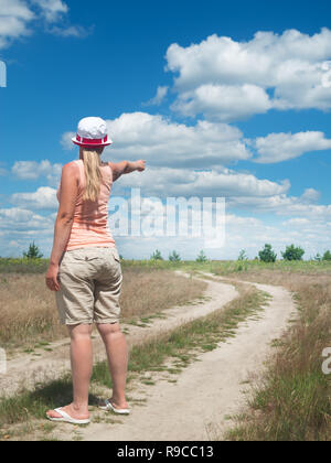 La jeune fille sur la route points son doigt quelque part dans la distance Banque D'Images