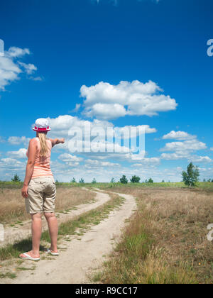 La jeune fille sur la route points son doigt quelque part dans la distance Banque D'Images