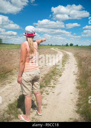 La jeune fille sur la route points son doigt quelque part dans la distance Banque D'Images