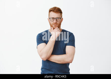 Creative smart businessman et penser à un nouveau concept d'entreprise. Portrait of handsome stratège ayant les cheveux rouges et de soies, de tenir la main sur la barbe et fixant l'accent de l'appareil photo Banque D'Images