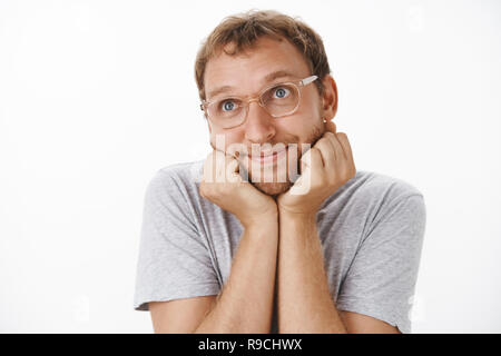 Tourné à l'intérieur d'adorables et tendres des profils guy dans les verres et les Grey T-shirt smiling avec délice la tête penchée sur les paumes et le regard sur l'angle supérieur gauche nostalgique et romanticly sur fond blanc Banque D'Images