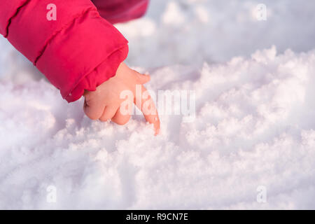 La main d'une petite fille écrit un doigt dans la neige sur une journée d'hiver ensoleillée. Banque D'Images