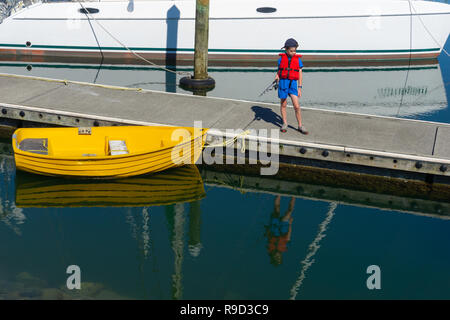 Petit garçon de marina pier fishingy canot jaune reflète dans l'eau. Banque D'Images