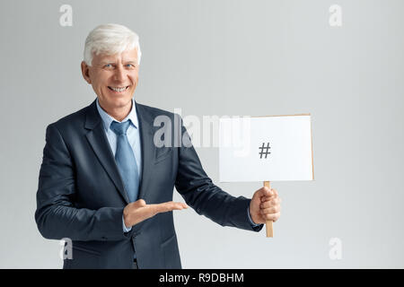 Senior business man studio isolés sur mur gris holding white board montrant dièse à la joyeuse souriante de l'appareil photo Banque D'Images