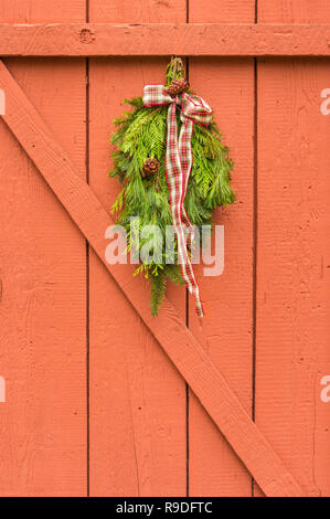 Evergreen naturelles traditionnelles avec swag Noël ruban à carreaux accrochées sur orange peint clôture de bois. Banque D'Images