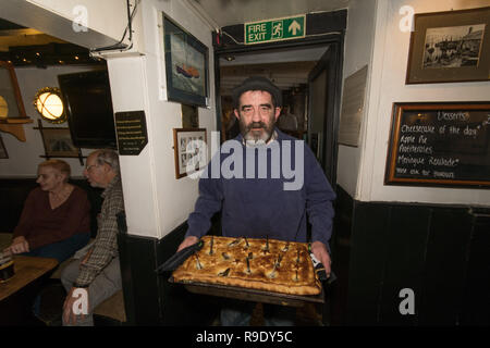 Mousehole, Cornwall, UK. Dec 23, 2018. 'Local' armes Madron comme Tom Bawcock Stargazy traditionnel faisant ressortir la tarte dans l'auberge de bateau à Mousehole. La tarte poisson avec têtes et queues de Sardine poussant hors de la Chambre, est servi dans le pub sur Tom Bawcocks Eve l'histoire raconte que Tom, un pêcheur du 16ème siècle, ont bravé les tempêtes et pris assez de poissons pour nourrir tout le village. Crédit : Simon Maycock/Alamy Live News Banque D'Images