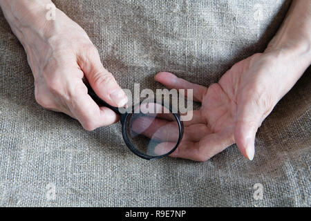 Mains d'une vieille femme tenant une loupe. Close-up. Banque D'Images
